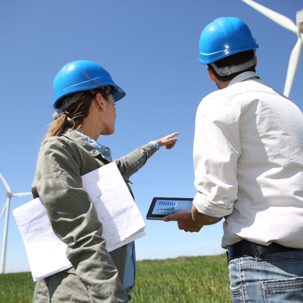 Eine Frau und ein Mann mit blauen Sicherheitshelmen inspizieren Windräder