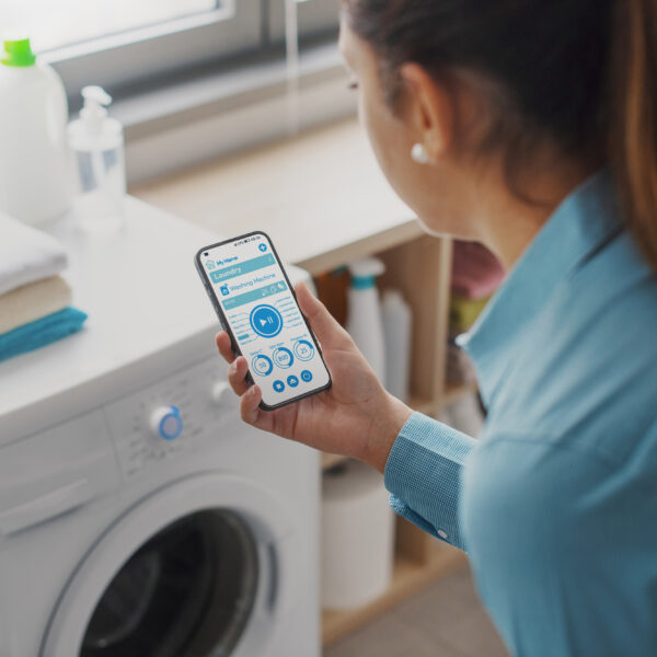 Frau prüft mittels Smartphone die Funktion der Waschmaschine